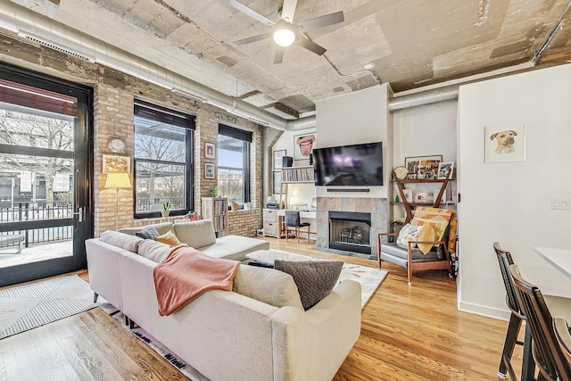 living room with baseboards, brick wall, ceiling fan, light wood-style floors, and a tiled fireplace