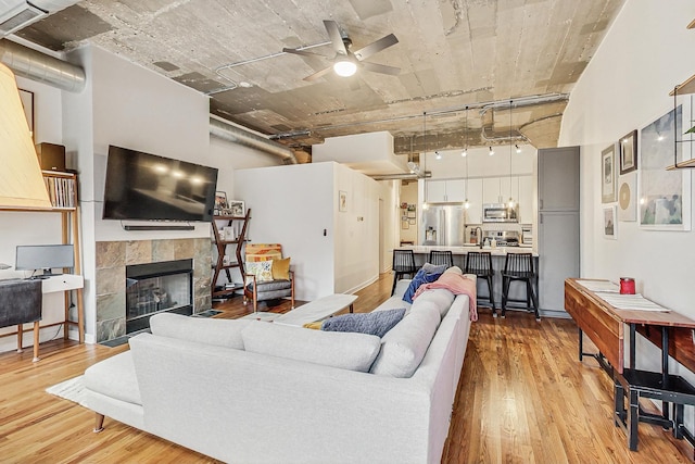 living area with a high ceiling, ceiling fan, a tiled fireplace, and light wood finished floors