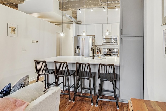 kitchen featuring wood finished floors, a sink, appliances with stainless steel finishes, a kitchen breakfast bar, and backsplash