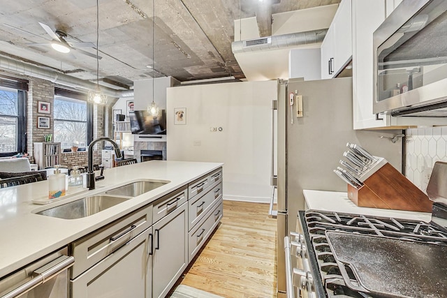 kitchen featuring a sink, light wood-style floors, appliances with stainless steel finishes, a fireplace, and hanging light fixtures