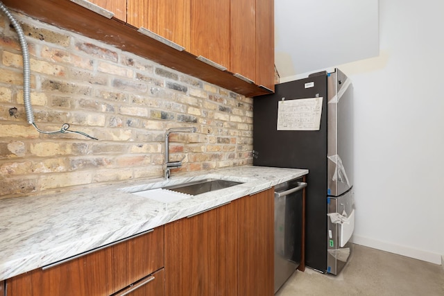 kitchen featuring brown cabinets, a sink, light stone counters, stainless steel dishwasher, and baseboards