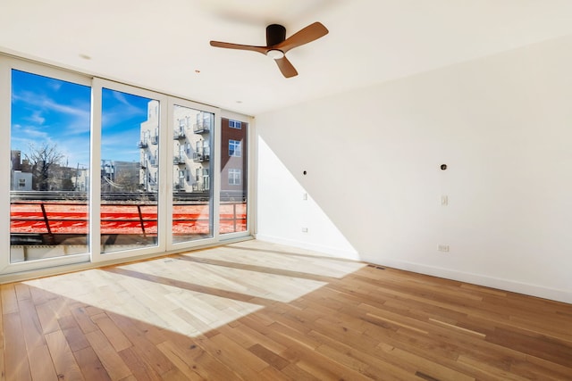 empty room featuring light wood-type flooring, baseboards, a view of city, and floor to ceiling windows