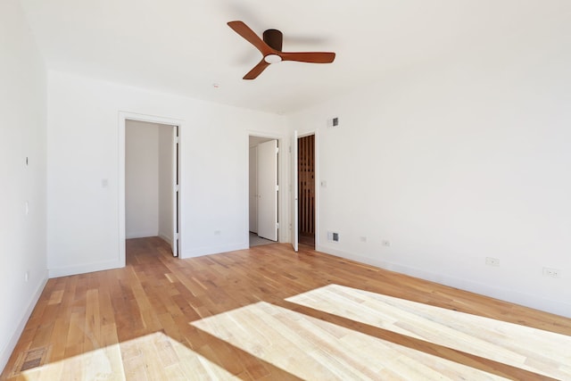 unfurnished bedroom with a walk in closet, visible vents, a ceiling fan, light wood-style floors, and baseboards