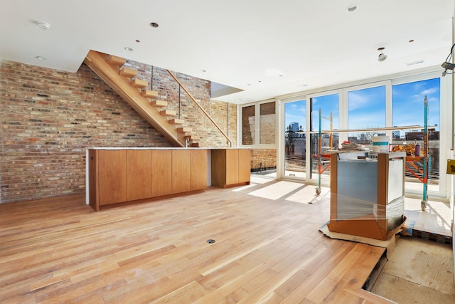 interior space featuring expansive windows, light wood-style floors, brick wall, and stairs