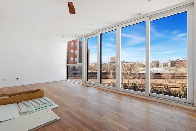 unfurnished room with visible vents, a ceiling fan, expansive windows, wood-type flooring, and baseboards