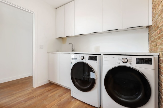 laundry room featuring light wood-type flooring, independent washer and dryer, cabinet space, brick wall, and baseboards