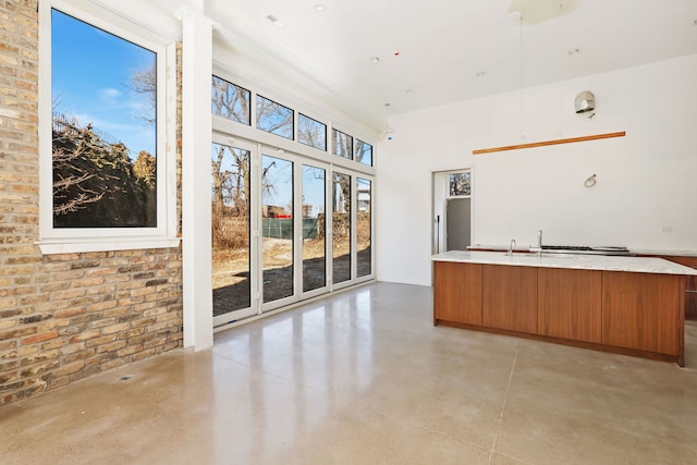 kitchen with finished concrete flooring, a center island with sink, light countertops, brown cabinets, and modern cabinets