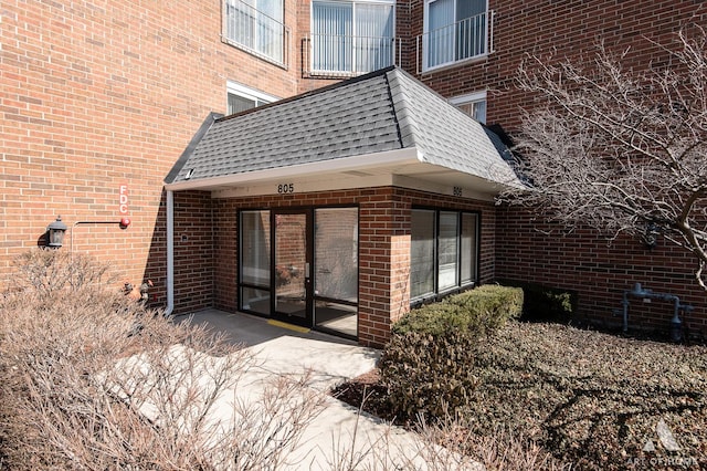 back of property with brick siding, mansard roof, and roof with shingles