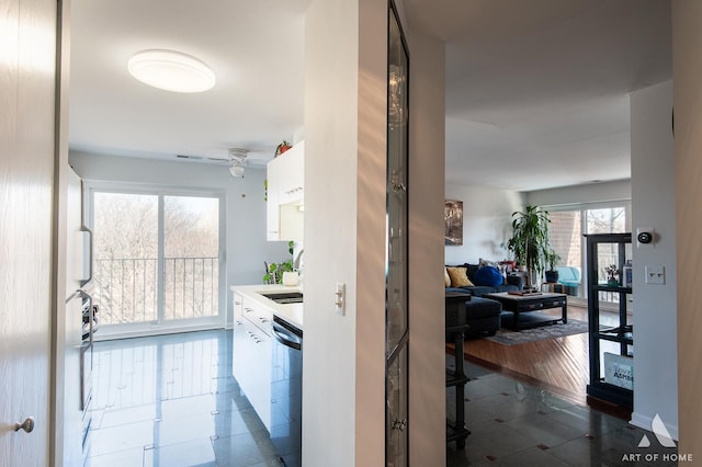 kitchen featuring ceiling fan, light countertops, stainless steel dishwasher, white cabinets, and a sink