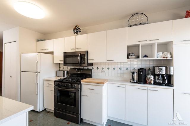 kitchen featuring stainless steel microwave, freestanding refrigerator, black gas stove, light countertops, and decorative backsplash