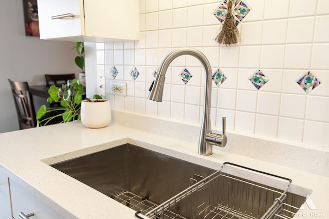 room details featuring light stone counters, decorative backsplash, white cabinetry, and a sink