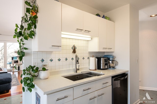 kitchen with backsplash, white cabinets, black dishwasher, and a sink