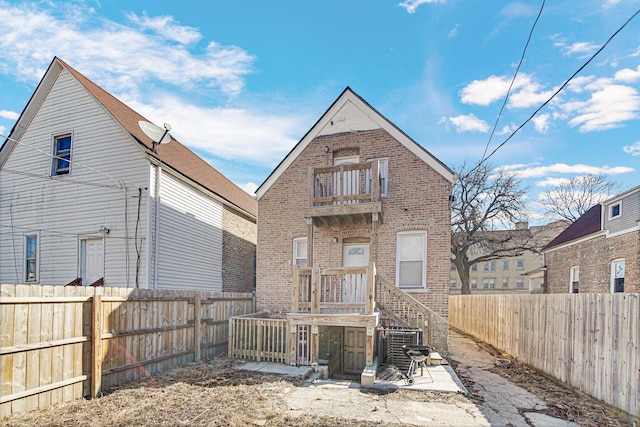 rear view of property with brick siding, a fenced backyard, central air condition unit, and a balcony