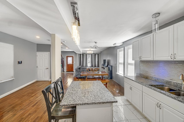 kitchen with decorative backsplash, baseboards, white cabinetry, and a sink