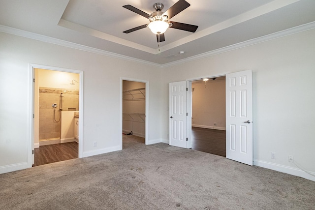 unfurnished bedroom with a raised ceiling, carpet floors, ensuite bath, and a spacious closet