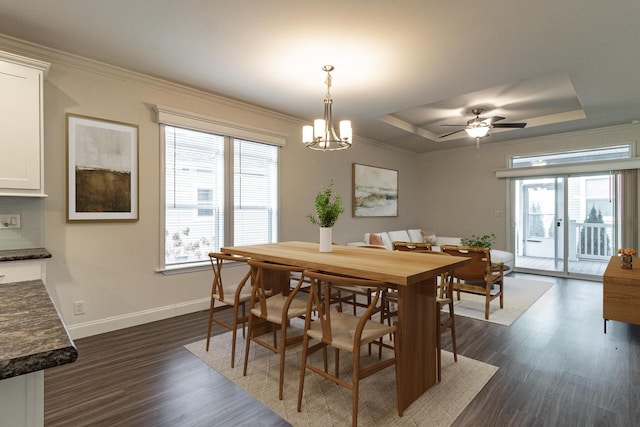 dining space featuring dark wood-type flooring, baseboards, crown molding, and a tray ceiling