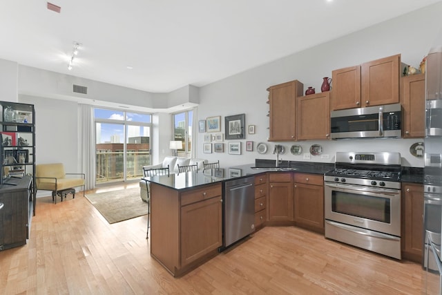 kitchen with visible vents, a peninsula, a sink, appliances with stainless steel finishes, and light wood-type flooring