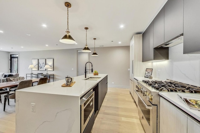 kitchen featuring an island with sink, recessed lighting, a sink, under cabinet range hood, and appliances with stainless steel finishes