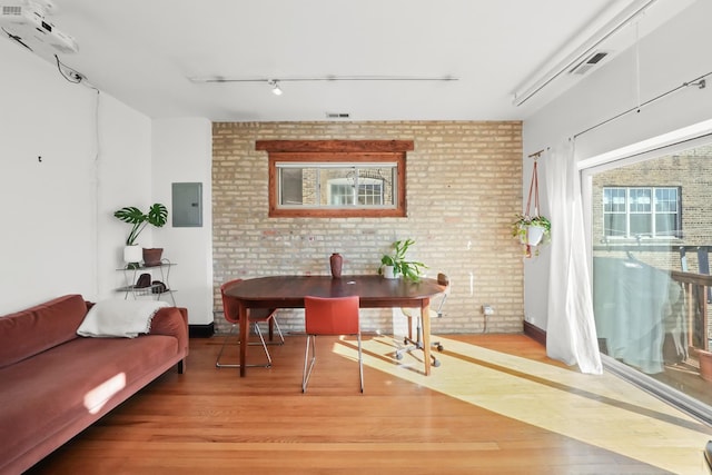 interior space featuring visible vents, brick wall, electric panel, track lighting, and light wood-type flooring