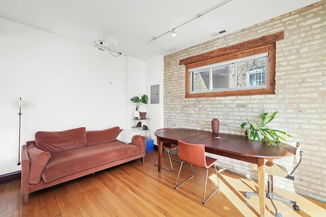 office with visible vents, electric panel, brick wall, rail lighting, and light wood finished floors