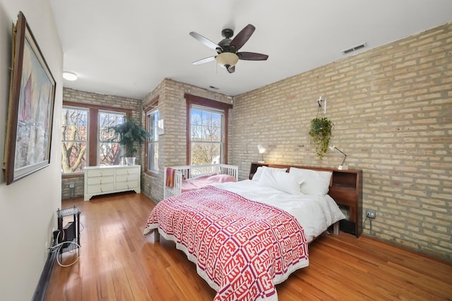 bedroom featuring visible vents, brick wall, ceiling fan, and wood finished floors