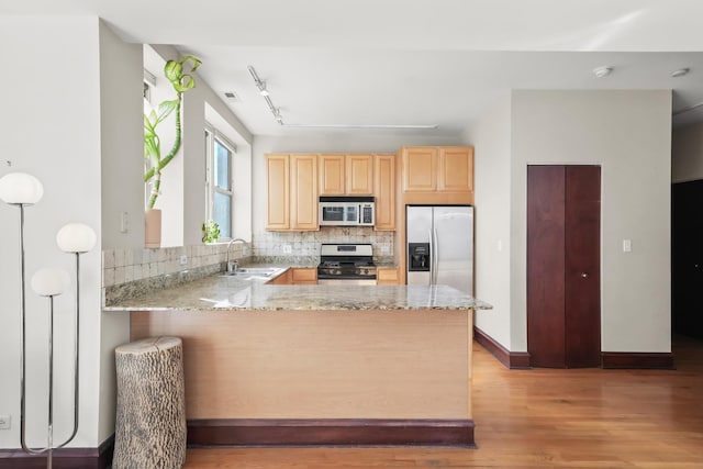 kitchen with light brown cabinets, a peninsula, a sink, appliances with stainless steel finishes, and tasteful backsplash