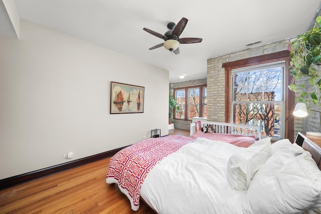 bedroom featuring a ceiling fan, visible vents, wood finished floors, and baseboards