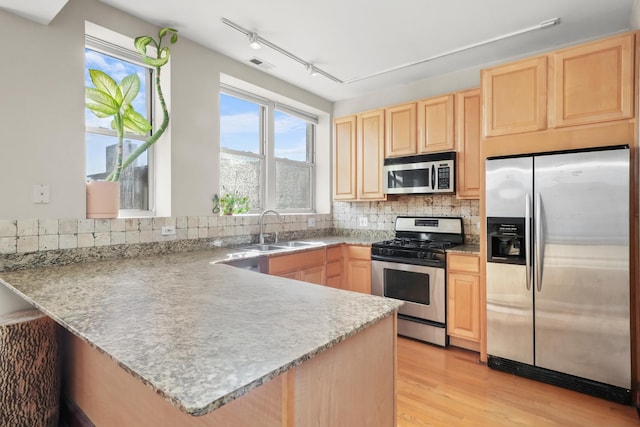 kitchen featuring light brown cabinets, a sink, light wood-style floors, appliances with stainless steel finishes, and a peninsula