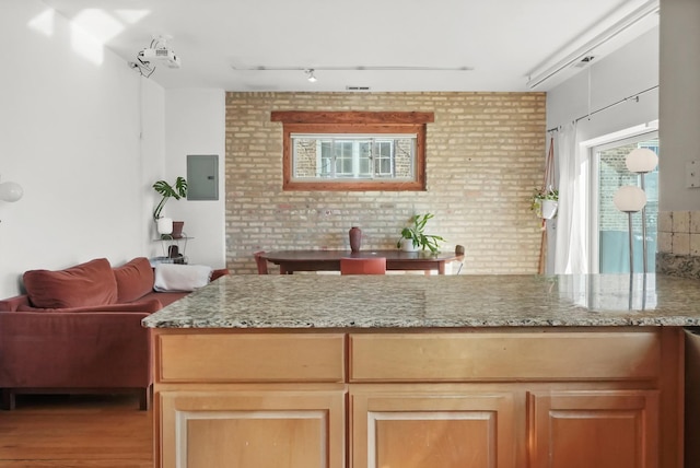 kitchen featuring light stone countertops, brick wall, electric panel, light wood-style floors, and open floor plan