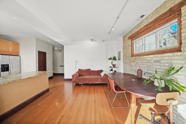 dining space featuring brick wall, light wood-style flooring, and track lighting