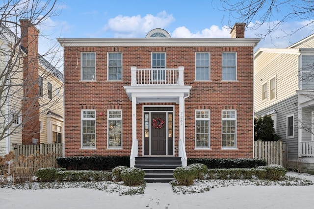 view of front of property featuring brick siding, a balcony, a chimney, and fence