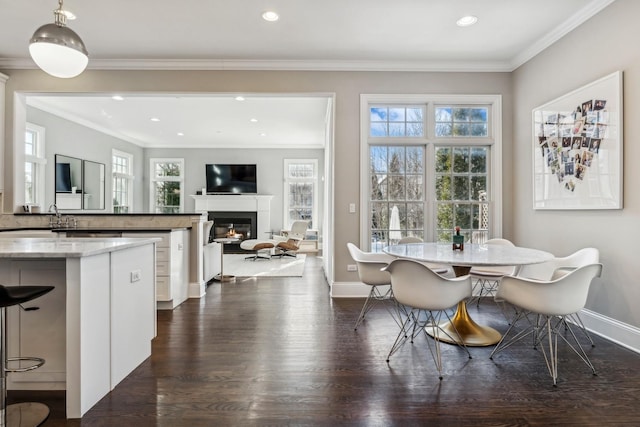 dining area with a glass covered fireplace, baseboards, dark wood finished floors, and ornamental molding