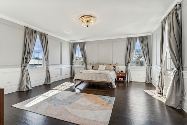 bedroom featuring a decorative wall, multiple windows, ornamental molding, and wood finished floors