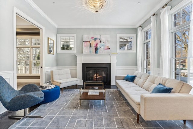 living room featuring a wainscoted wall, a glass covered fireplace, and ornamental molding