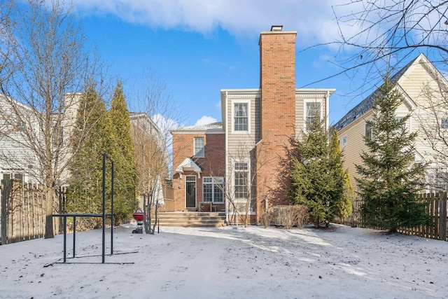 snow covered house featuring brick siding, a chimney, and fence