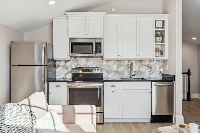 kitchen featuring a sink, decorative backsplash, vaulted ceiling, stainless steel appliances, and white cabinetry