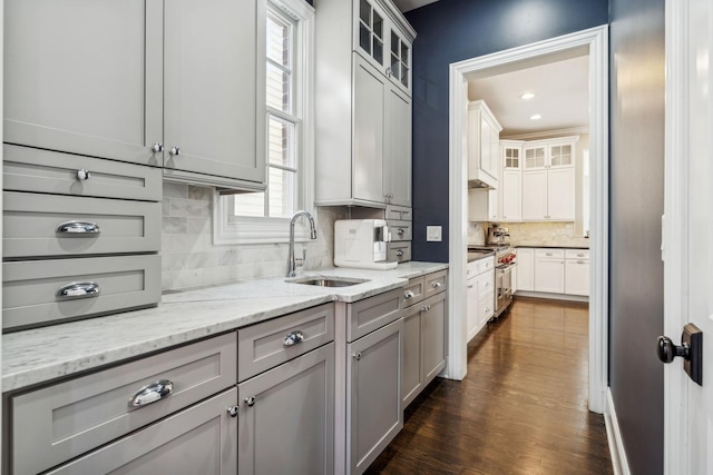 kitchen with backsplash, dark wood finished floors, light stone counters, high end stainless steel range, and a sink