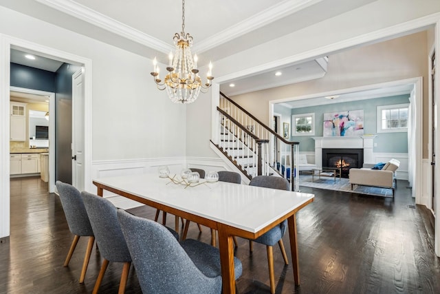 dining room with a glass covered fireplace, stairway, dark wood-style floors, and a wainscoted wall