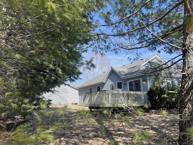 view of side of home with roof with shingles and a wooden deck