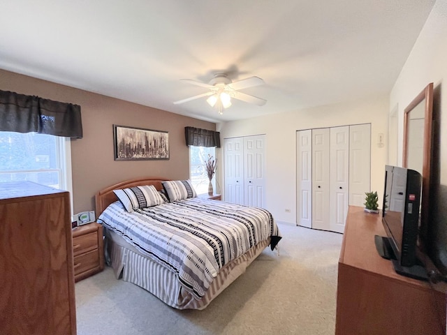 bedroom with light colored carpet, a ceiling fan, and multiple closets