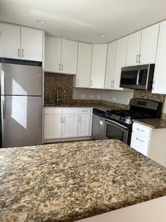 kitchen featuring light stone counters, stainless steel appliances, backsplash, and white cabinetry