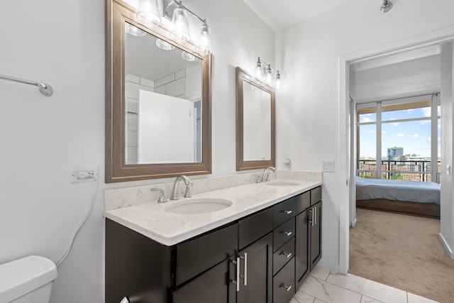 ensuite bathroom featuring double vanity, marble finish floor, toilet, and a sink