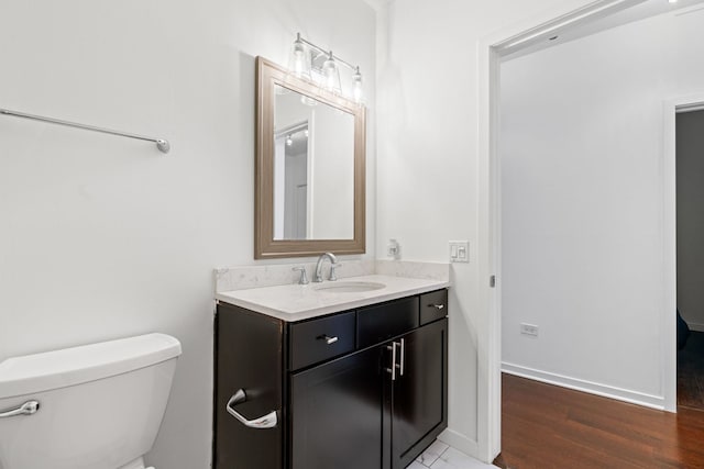 bathroom featuring baseboards, toilet, wood finished floors, and vanity