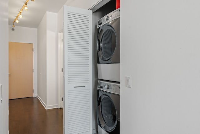 laundry area featuring baseboards, laundry area, rail lighting, stacked washing maching and dryer, and dark wood-style floors