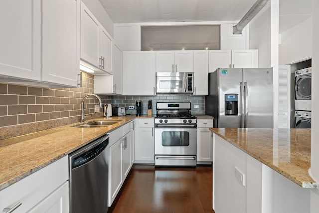 kitchen with a sink, backsplash, white cabinetry, stainless steel appliances, and stacked washer / drying machine