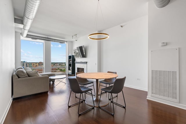 dining area featuring a fireplace, a wall of windows, baseboards, and dark wood-style flooring