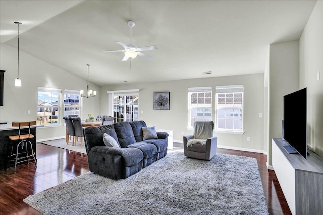 living area with visible vents, ceiling fan with notable chandelier, dark wood finished floors, baseboards, and vaulted ceiling