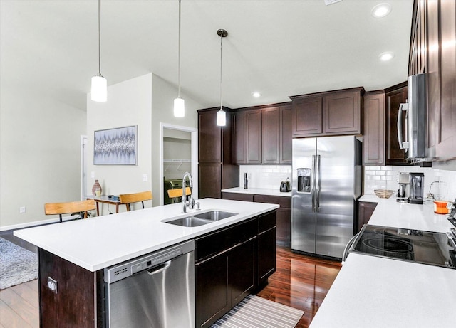 kitchen featuring a center island with sink, a sink, stainless steel appliances, dark wood-type flooring, and light countertops