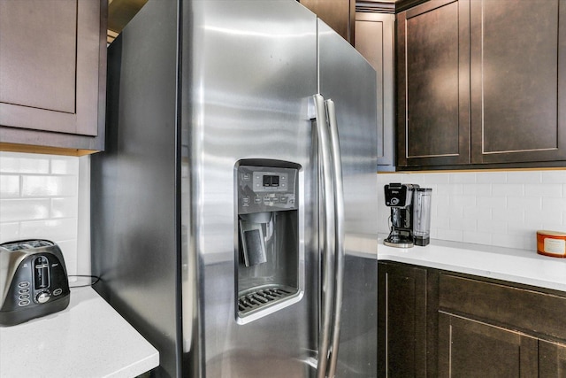 kitchen with stainless steel fridge, tasteful backsplash, dark brown cabinets, and light countertops