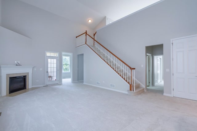 unfurnished living room featuring carpet, visible vents, high vaulted ceiling, a fireplace with flush hearth, and stairs